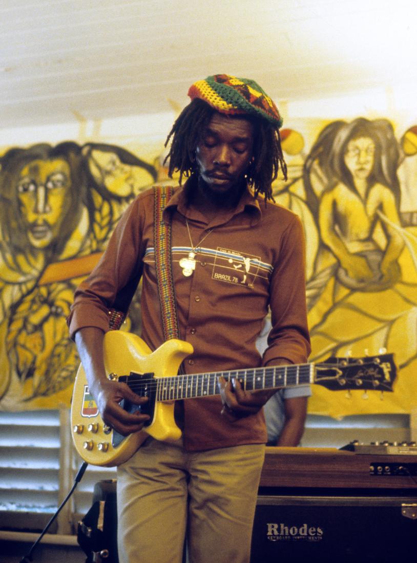 Peter Tosh playing guitar in front of a painted mural